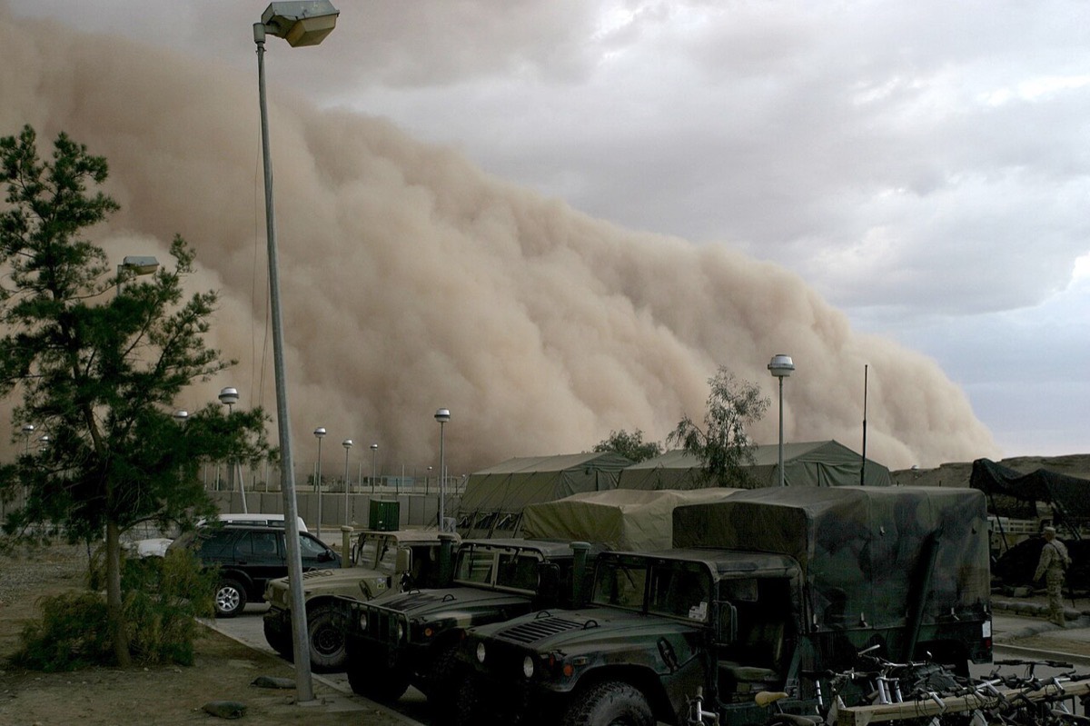 A towering wall of brown dust rolling over buildings and vehicles