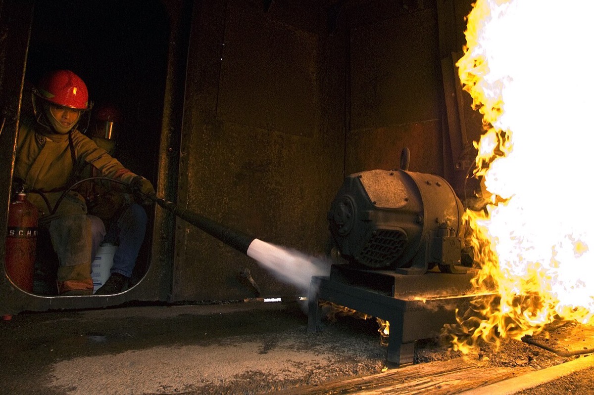 Trainee discharging a fire extinguisher at the base of a live training fire