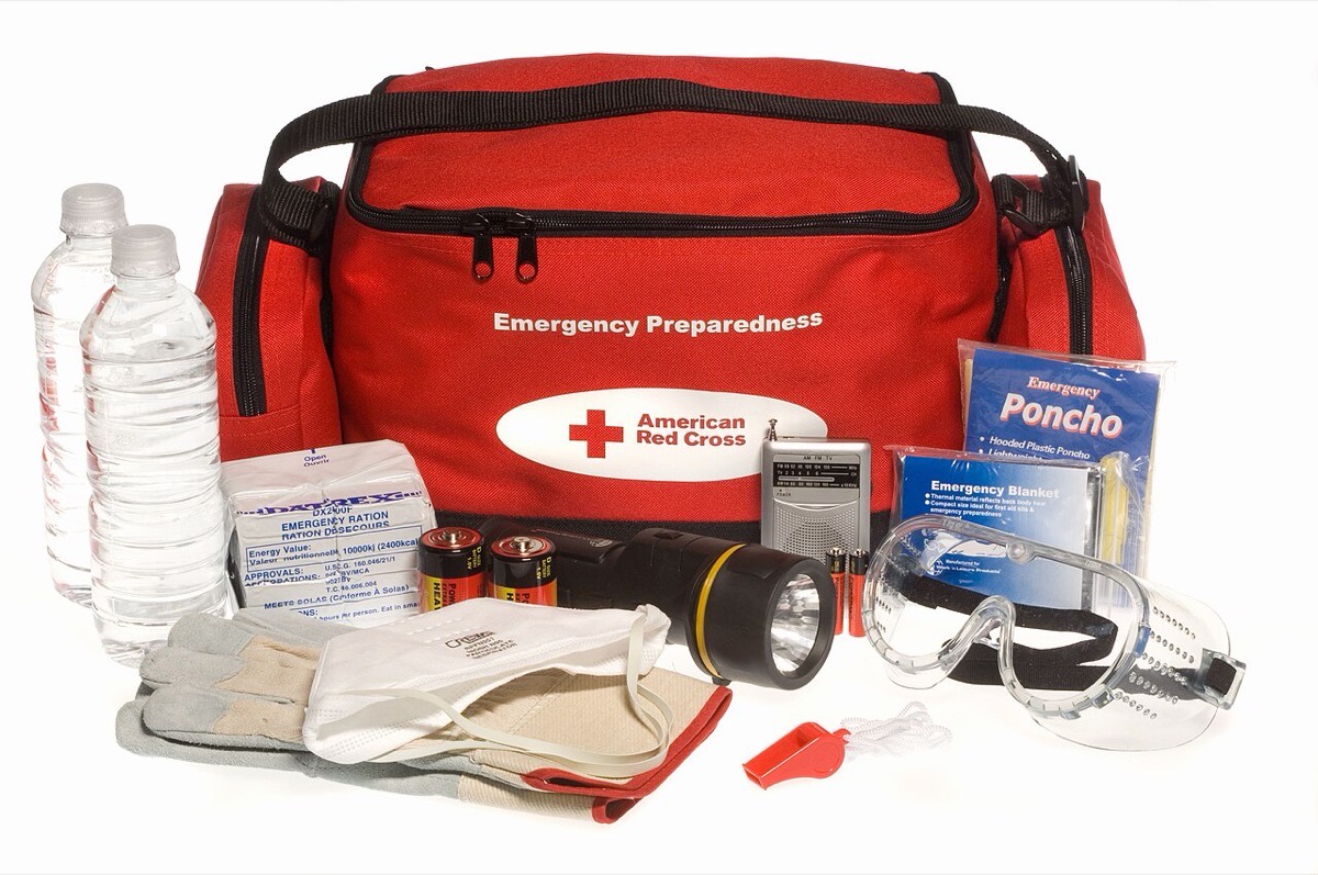Emergency go-kit with contents laid out: water bottles, radio, torch, batteries, gloves, dust mask, whistle, goggles, emergency blanket, poncho, and ration bars