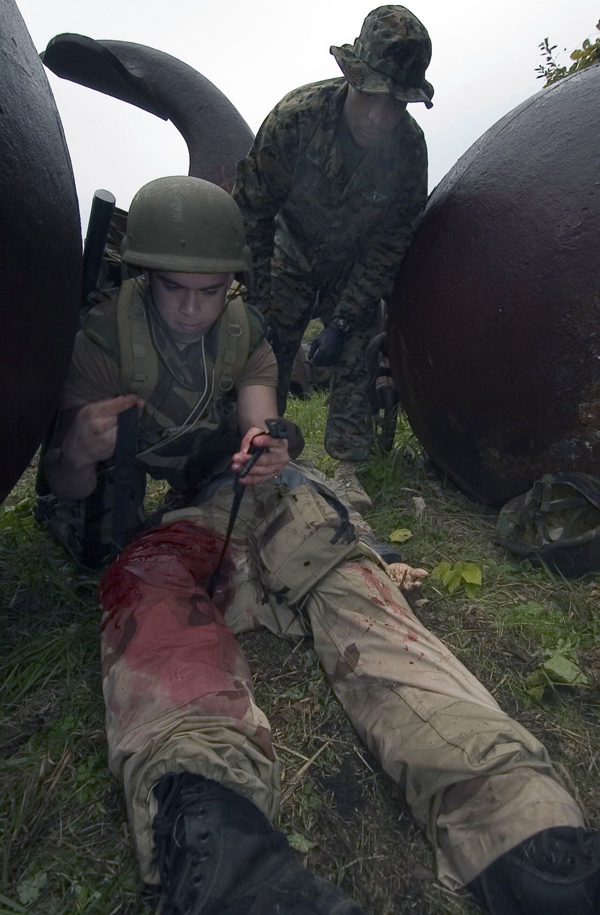 Soldier tightening a windlass tourniquet high on the thigh of a training casualty with a simulated leg wound
