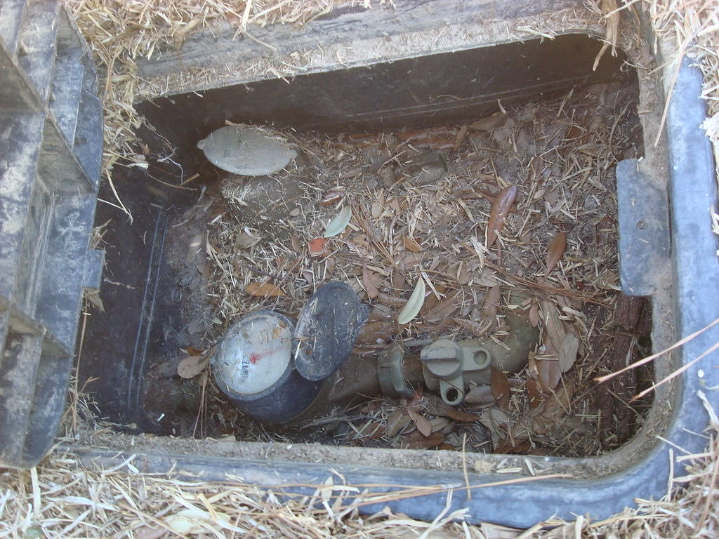Water meter and shutoff valve inside an in-ground meter box with the lid opened